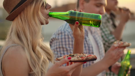 A-women-eat-pieces-of-hot-pizza-and-drink-beer-from-a-green-glass-bottle-on-the-party-with-his-friend-in-hot-summer-day.